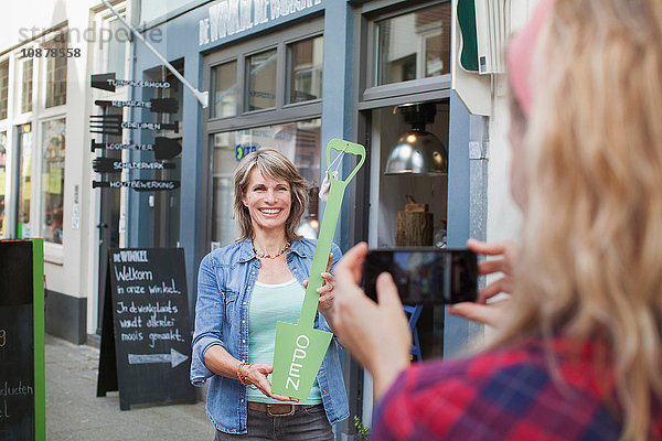 Freund fotografiert Frau vor einem Laden  der ein Schild offen hält