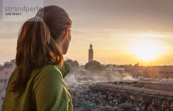 Rückansicht einer Frau  die den Sonnenuntergang über dem Platz Jemaa el-Fnaa  Marrakesch  Marokko  betrachtet