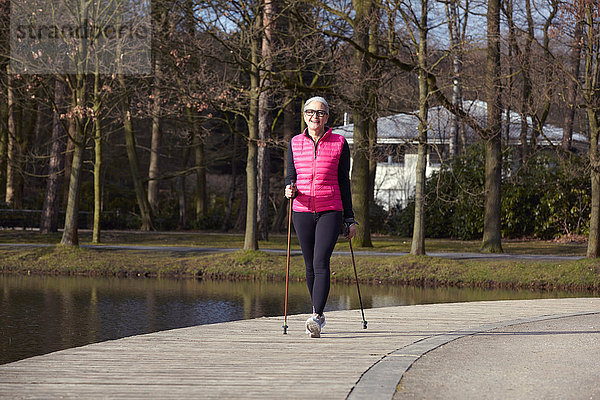 Vorderansicht einer Nordic-Walking-Frau am Teich in voller Länge