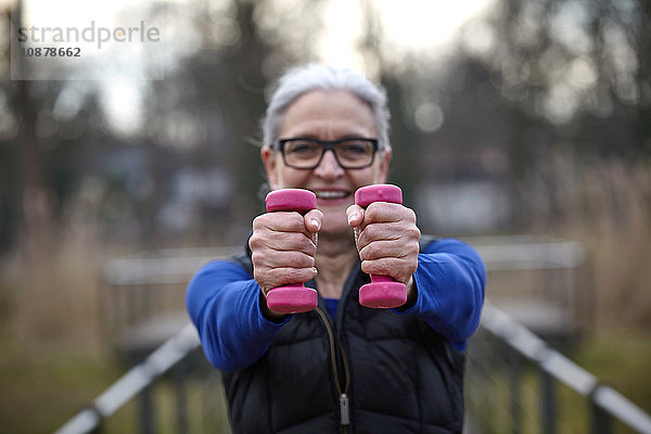 Frau mit Brille hält rosa Kurzhanteln in der Hand und schaut lächelnd in die Kamera