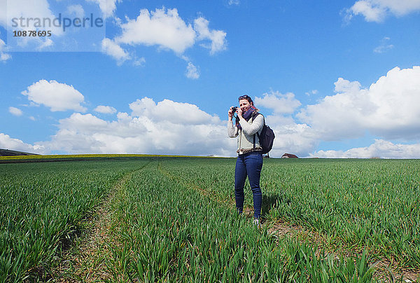 Junge Frau steht im Feld und fotografiert eine Landschaft