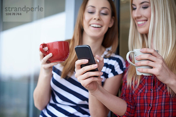 Zwei Freundinnen  Kaffee trinken  im Freien  Smartphone anschauen