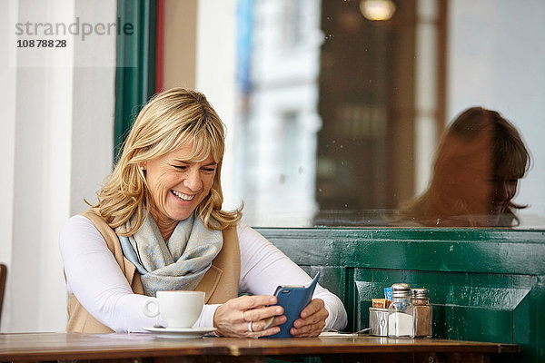 Reife Frau liest Smartphone-Text am Tisch im Straßencafé