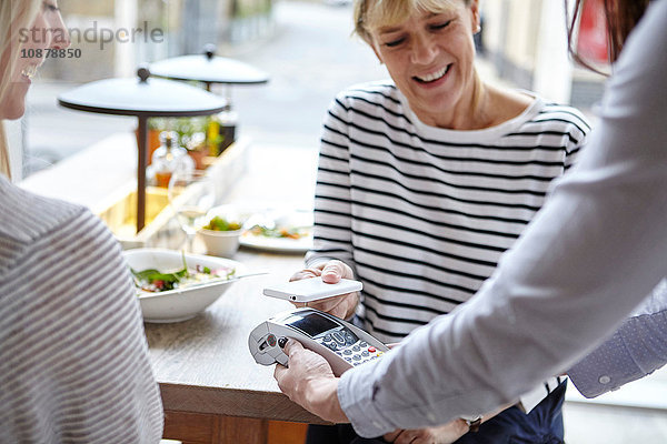 Frau benutzt kontaktloses Bezahlen per Smartphone am Restauranttisch  London  UK