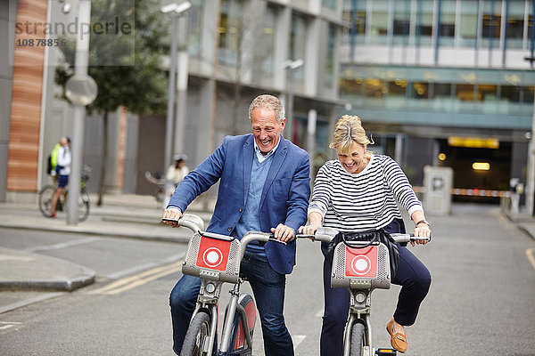 Älteres Pärchen  das lacht  während es auf Leihfahrrädern Fahrrad fährt  London  UK