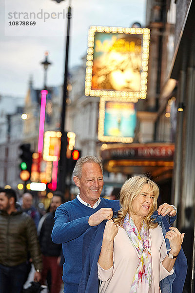 Ein reifer Mann zieht seiner Freundin in der Abenddämmerung auf der Straße in der Stadt die Jacke über die Schulter  London  Großbritannien
