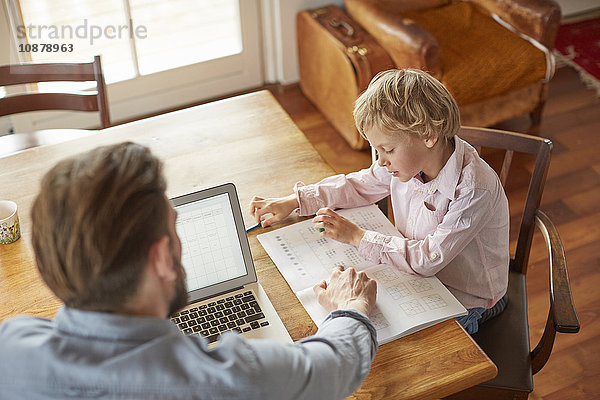 Vater hilft Sohn bei den Hausaufgaben im Home Office