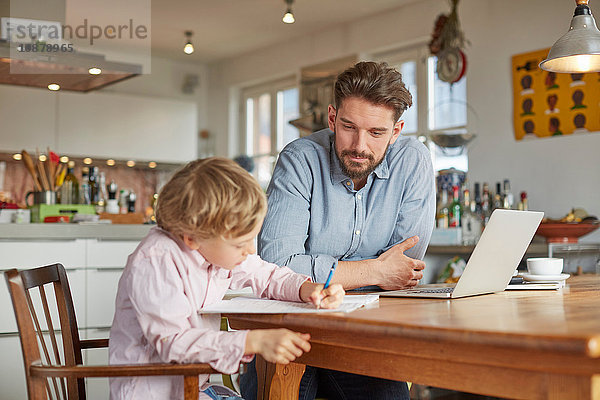 Vater hilft Sohn bei den Hausaufgaben im Home Office