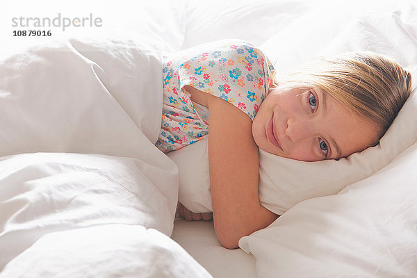Porträt eines blondhaarigen Mädchens  das im Bett ein Kissen umarmt