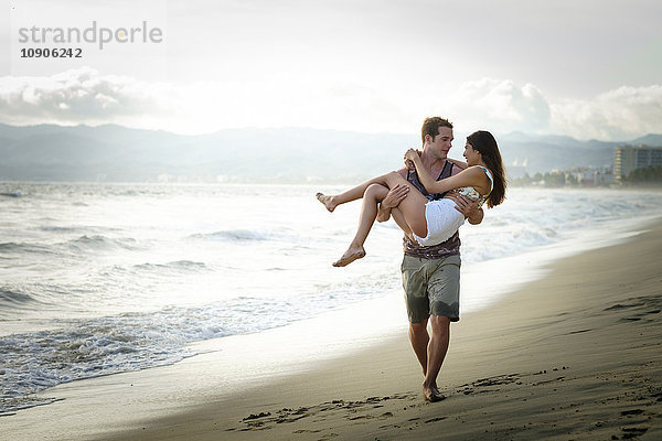 Mann trägt seine Freundin am Strand.