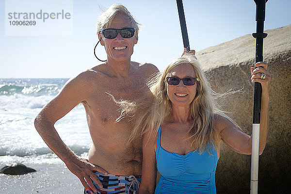Portrait of happy senior couple holding paddles by the sea