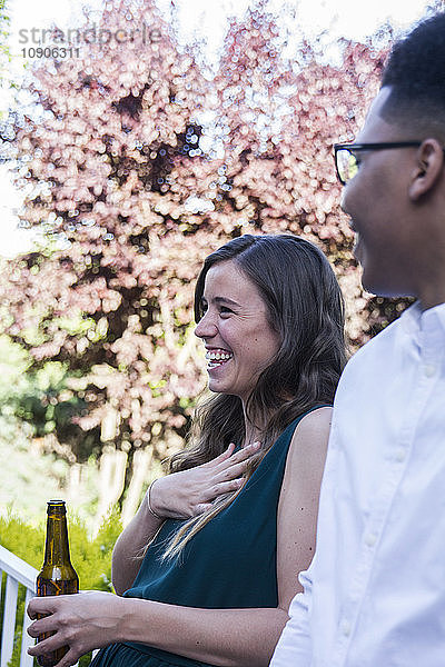 Woman laughing  drinking a bottle of beer during a summer dinner in a garden