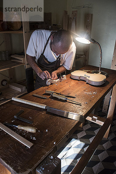 Luthier using a chisel on a violin scroll during the manufacture of a violin in his workshop