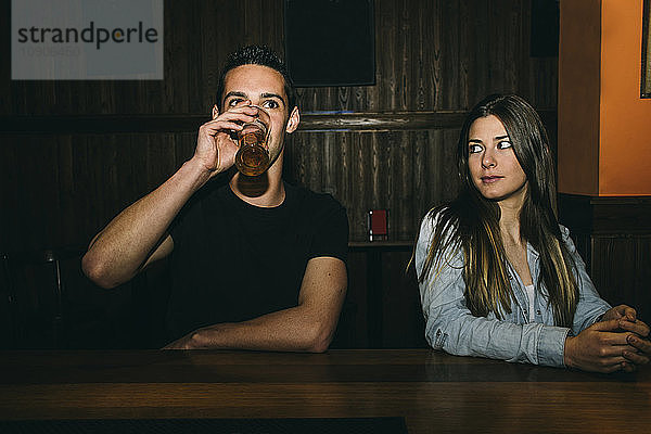 Man drinking beer at the bar counter while woman looks at him