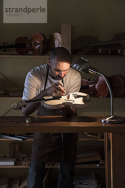 Luthier examining the sound post of an unvarnished violin in his workshop