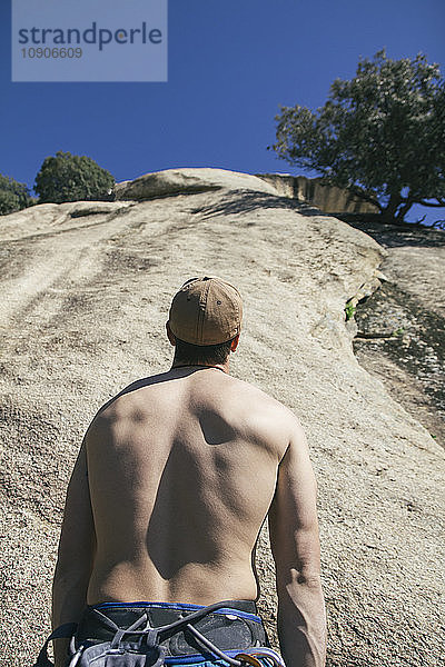 Back of a shirtless man with a gap looking at a wall before climbing