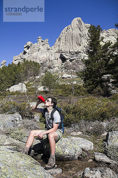 Spain  hiker with sunglasses and backpack drinking from bottle sitting on a rock in La Pedriza
