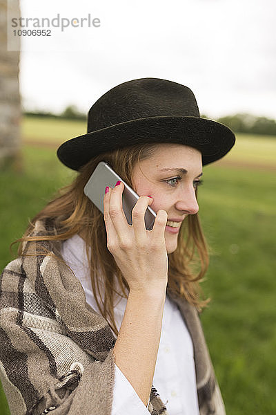 Young woman wearing hat telephoning with smartphone at countryside