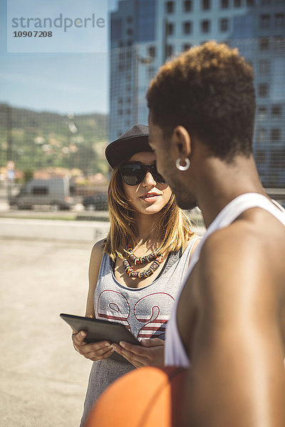 Junge Frau mit digitalem Tablett im Gespräch mit einem Basketballspieler