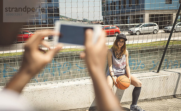 Junger Mann fotografiert junge Frau auf dem Basketballplatz