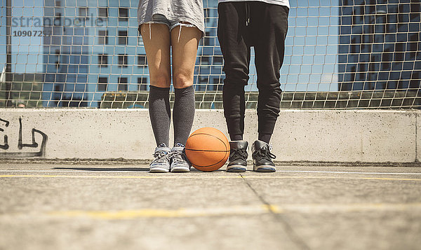 Junger Mann und Frau stehen auf dem Basketballfeld mit zwischen den Füßen.