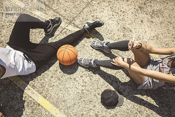 Junges Paar am Boden sitzend mit Basketball und Smartphone