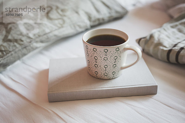 Buch und Tasse schwarzen Kaffee auf einem Bett
