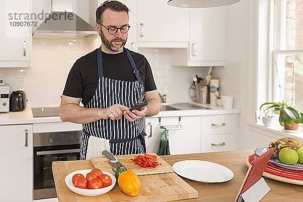 Portrait of man using smartphone while preparing food in the kitchen