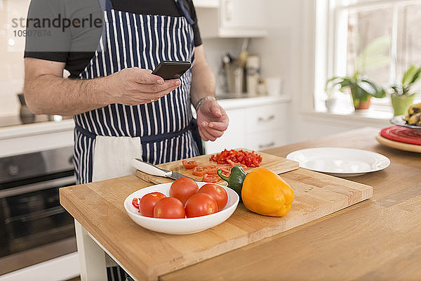 Man using smartphone while preparing food in the kitchen  partial view