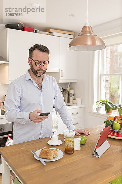 Man standing in his kitchen in the morning looking at his smartphone