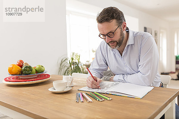 Man with colouring book and coloured pencils sitting at wooden table