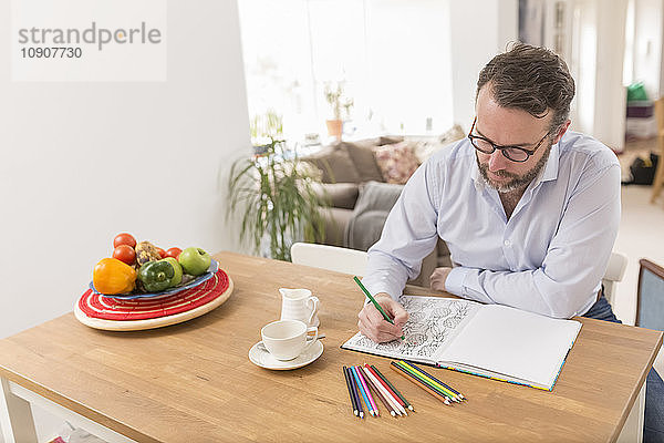 Man sitting at wooden table with colouring book and coloured pencils