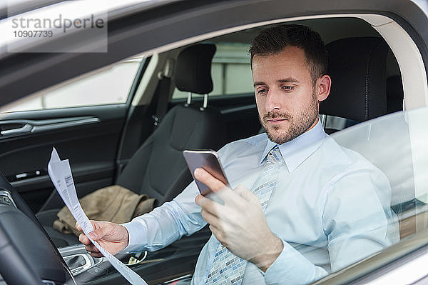 Businessman with documents and cell phone in car