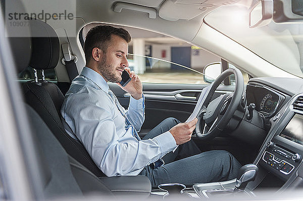 Businessman with documents on cell phone in car