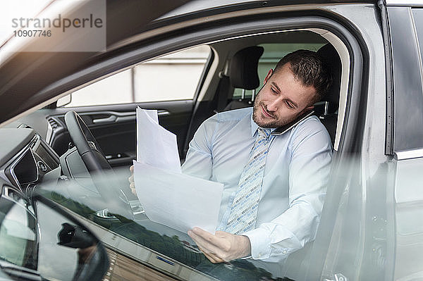 Businessman with documents on cell phone in car
