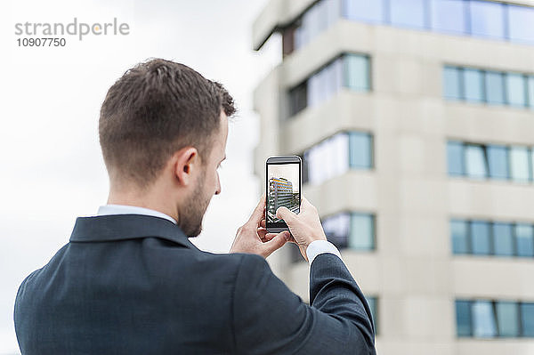 Businessman taking a cell phone picture of an office building