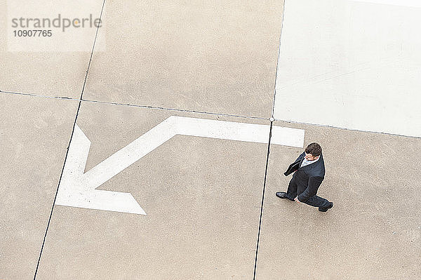 Businessman walking on paving with large arrow