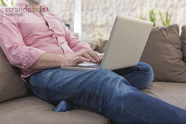 Mature man sitting on couch using laptop