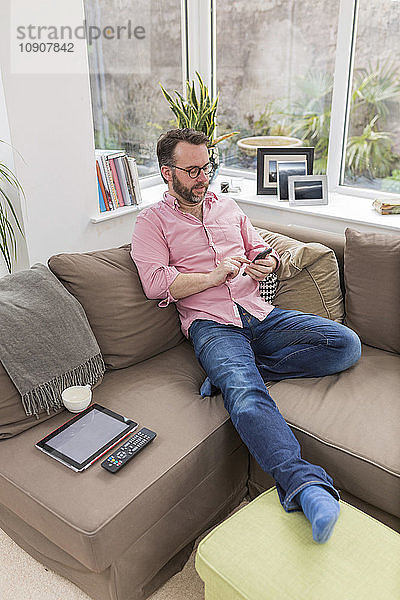 Mature man sitting on couch using smart phone