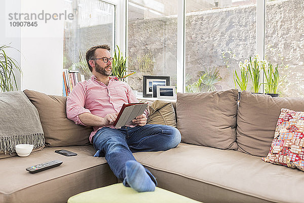 Mature man sitting on couch using digital tablet