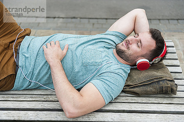Relaxed young man lying on bench listening to music