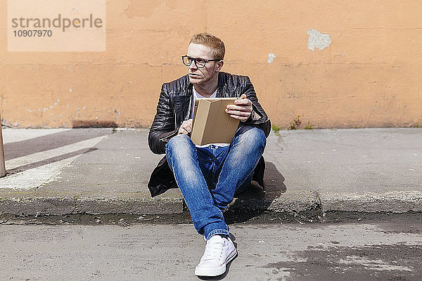 Young man with digital tablet sitting at curb
