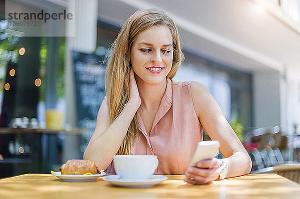 Portrait of smiling woman sitting in a sidewalk cafe looking at her smartphone