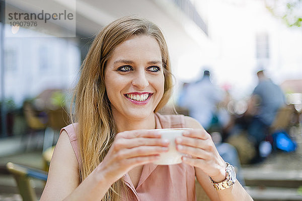 Portrait of smiling woman sitting in a sidewalk cafe with cup of coffee
