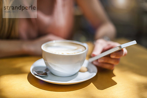 Woman sitting in a coffee shop with Cappuccino holding smartphone  close-up