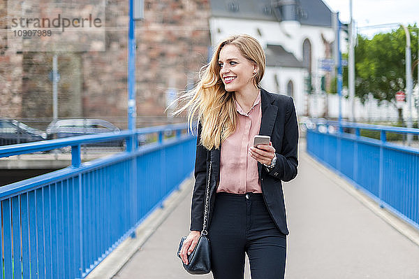 Smiling businesswoman walking on a bridge looking at her smartphone