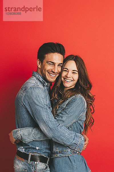 Portrait of happy young couple hugging each other in front of red background