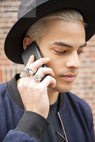 Portrait eines jungen Mannes mit Ringen und Huttelefonie mit Smartphone