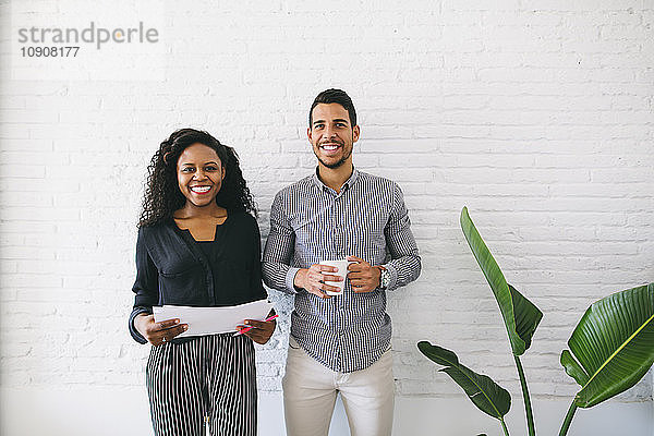 two young business people standing against wall  haolding papers and cup of coffee