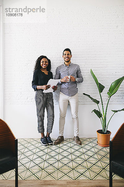 two young business people standing against wall  haolding papers and cup of coffee